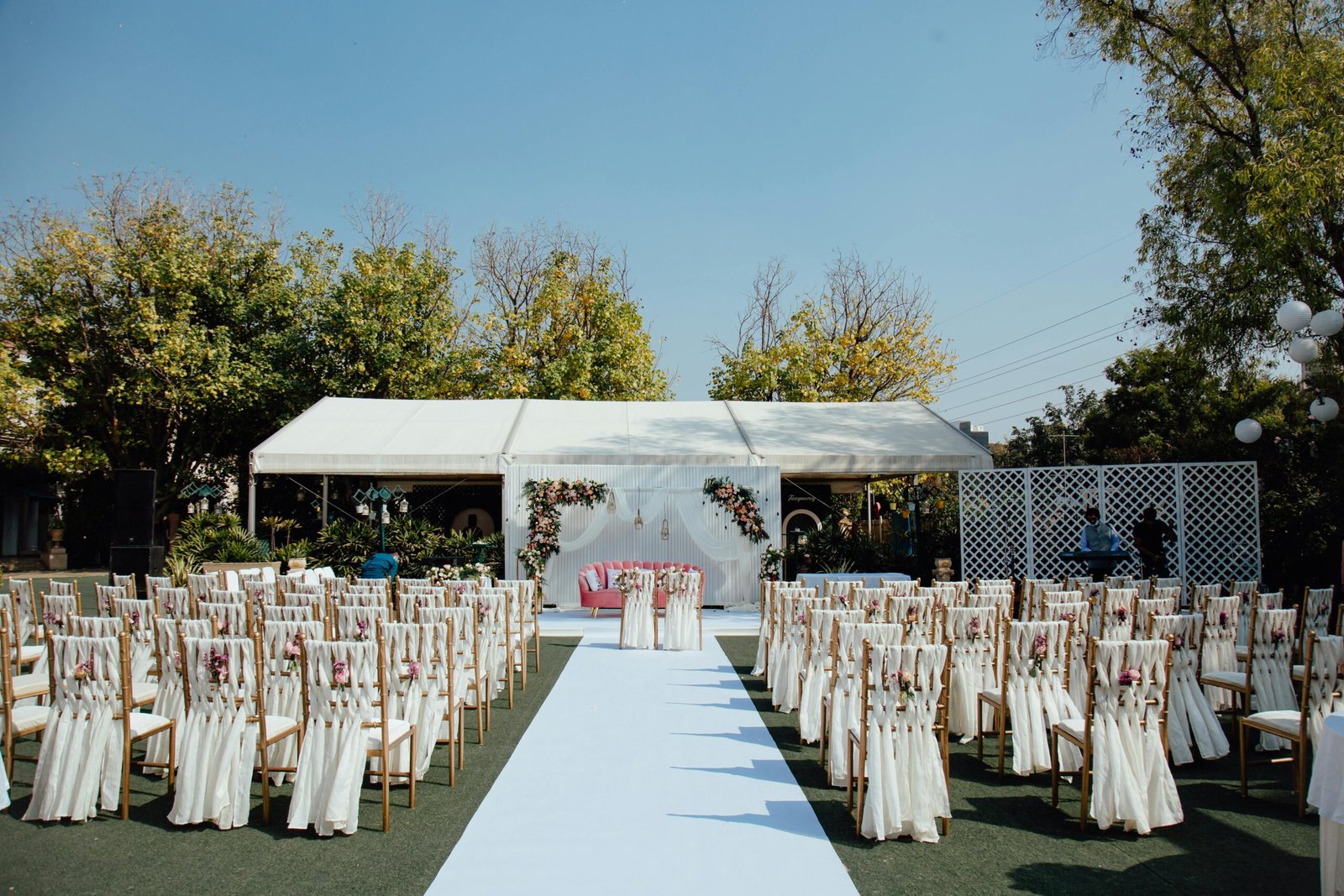 Elegant outdoor wedding setup with decorated chairs and floral arrangements under a clear blue sky.